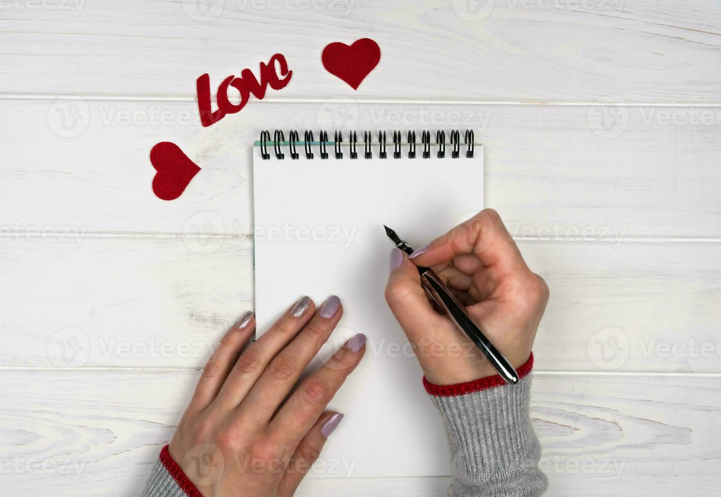 Woman's hand writes love message on notepad. Flatlay composition. Love romantic message for Valentine's Day. Valentine's Day holiday concept. Top view. photo