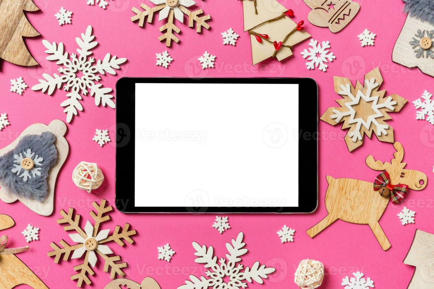 Top view of digital tablet on pink background made of holiday decorations and toys. Christmas ornament concept photo