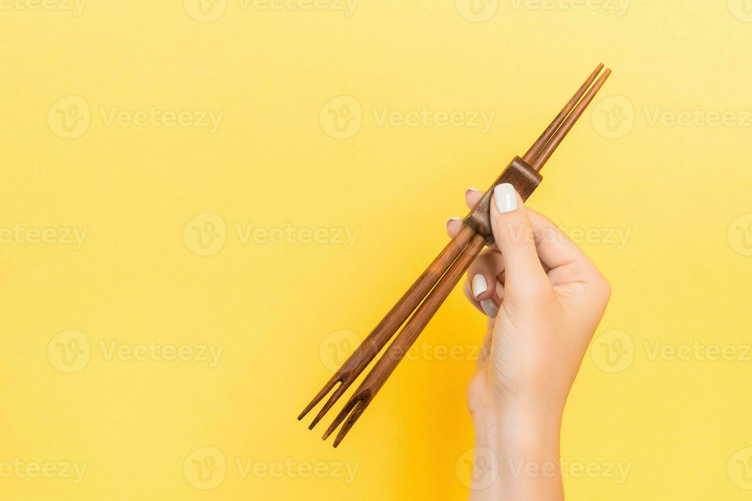 Female hand holding chopsticks on yellow background. Sushi concept with empty space for your idea photo