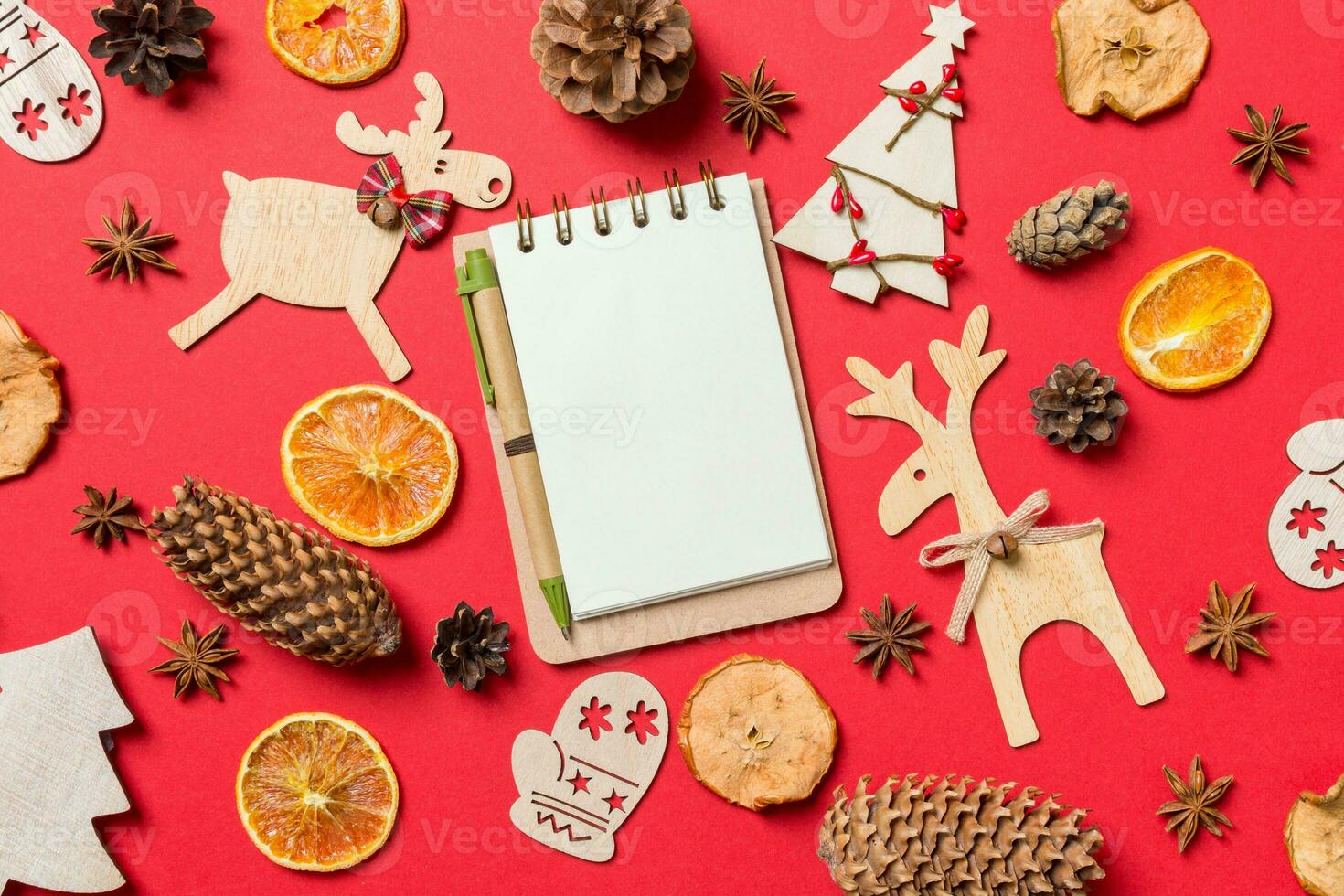 Top view of notebook, red background decorated with festive toys and Christmas symbols reindeers and New Year trees. Holiday concept photo