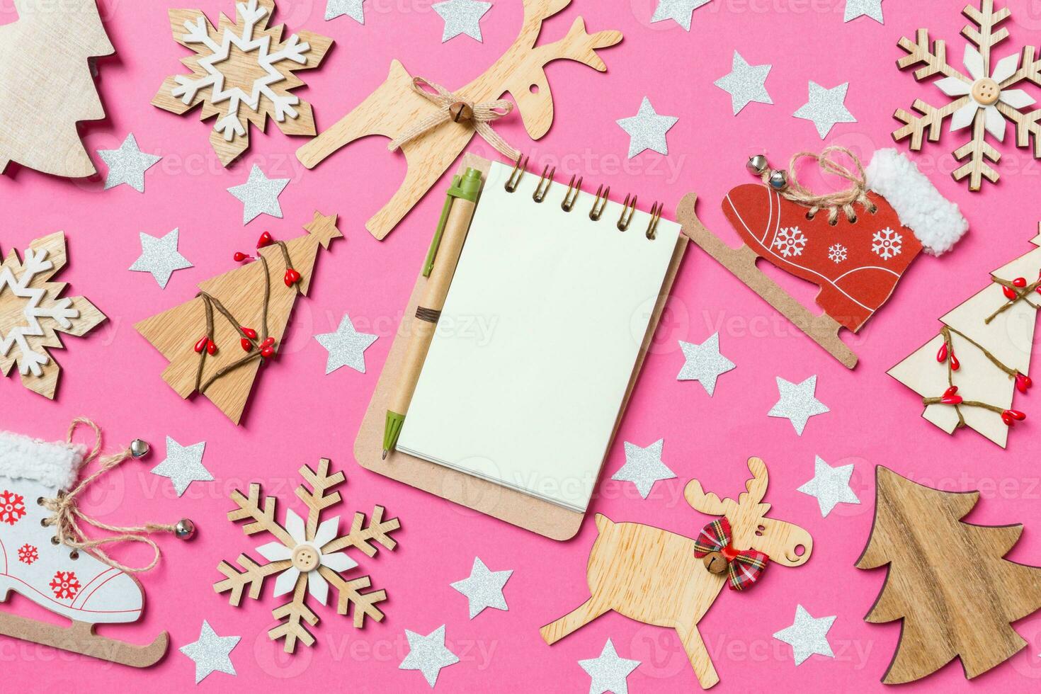 Top view of notebook, pink background decorated with festive toys and Christmas symbols reindeers and New Year trees. Holiday concept photo