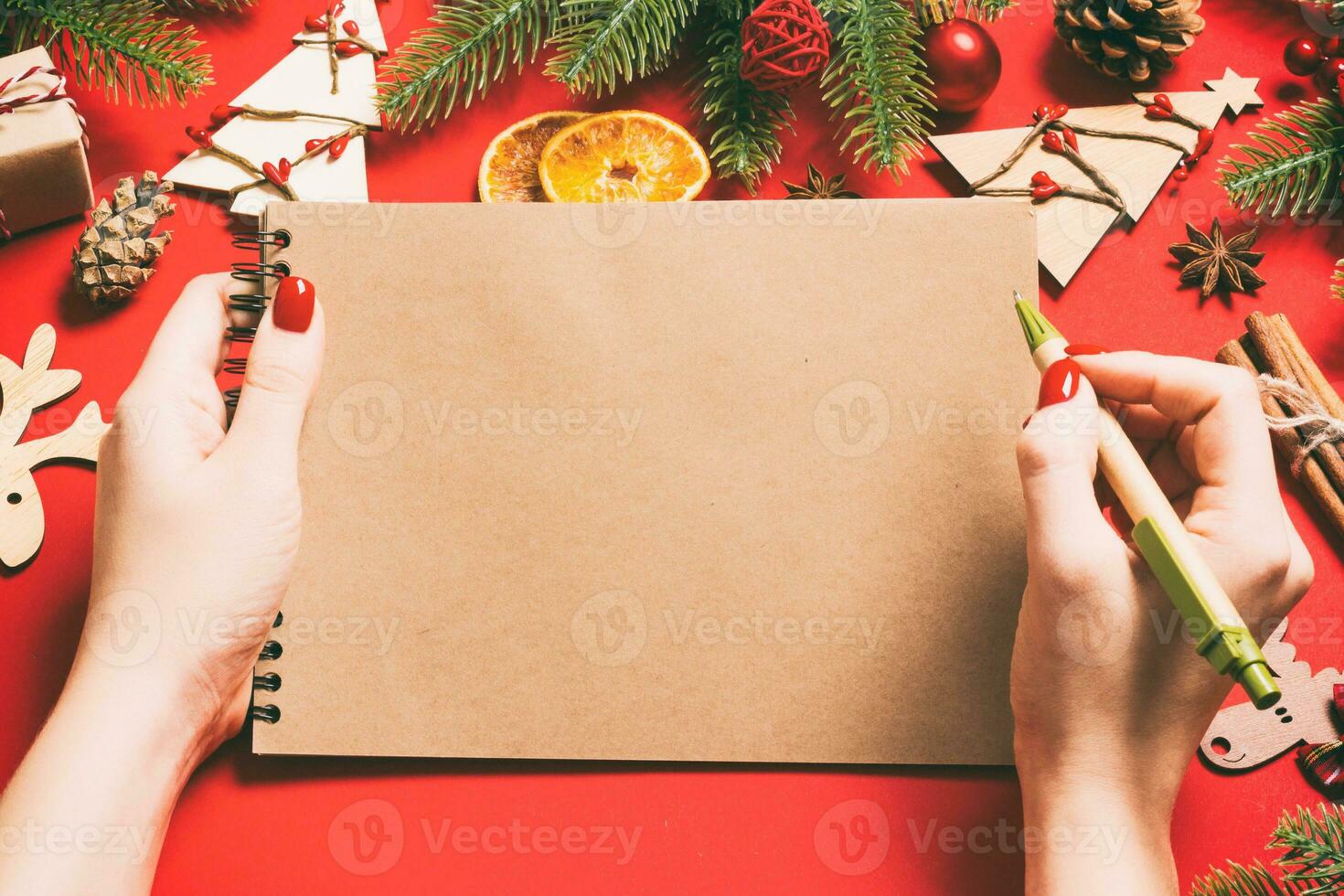 Top view of female hand making some notes in noteebok on red background. New Year decorations and toys. Christmas time concept photo