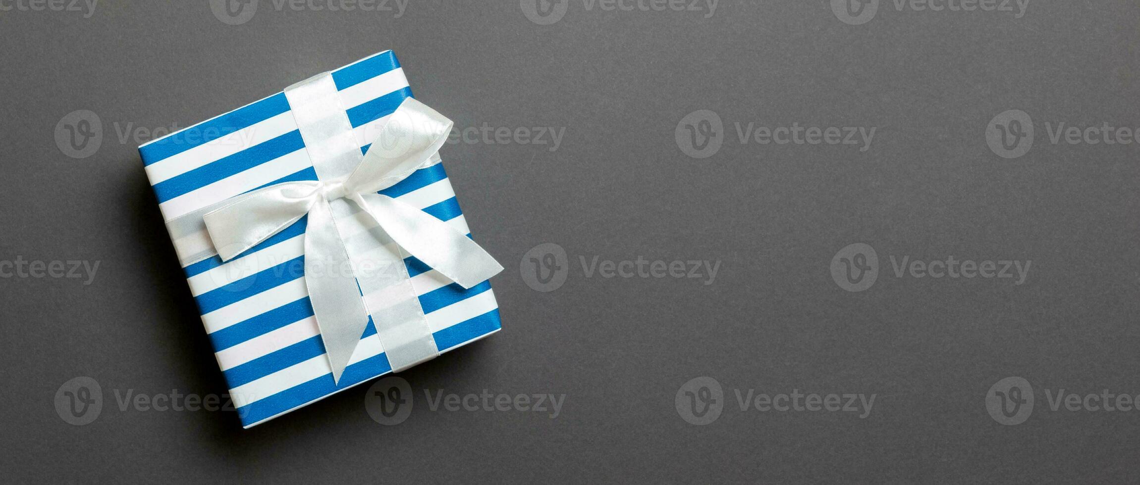 wrapped Christmas or other holiday handmade present in paper with white ribbon on black background. Present box, decoration of gift on colored table, top view with copy space photo