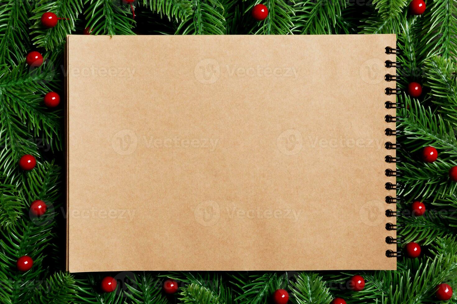 Top view of notebook made of craft paper decorated with a frame made of fir tree on wooden background. New Year time concept photo