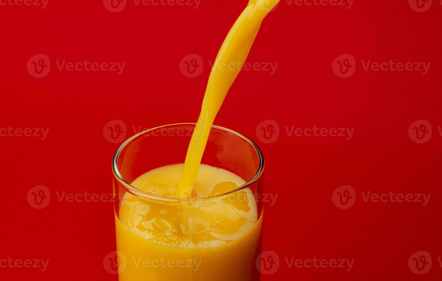 Orange juice pouring into glass, isolated on red background photo