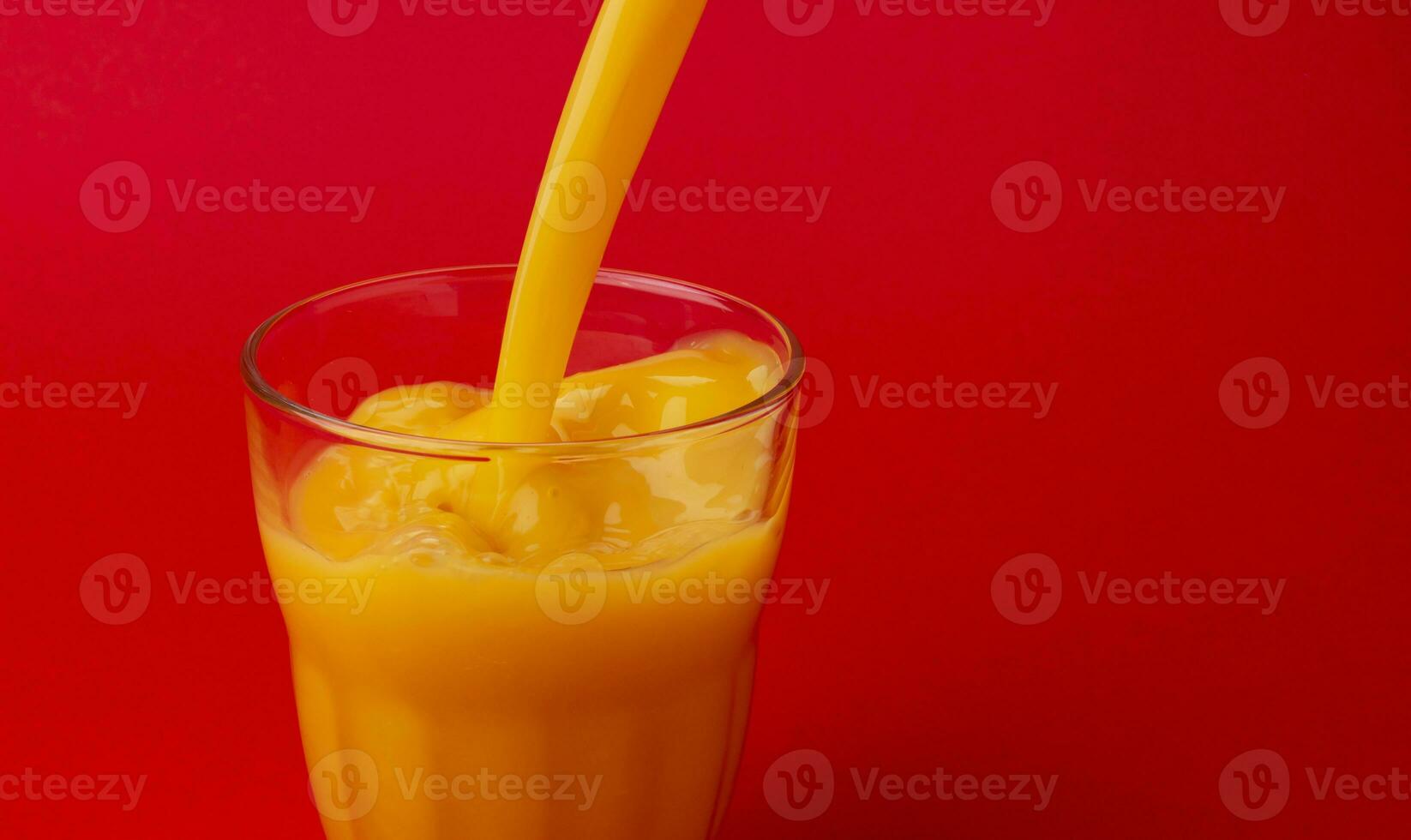 Orange juice pouring into glass, isolated on red background, with copy space photo