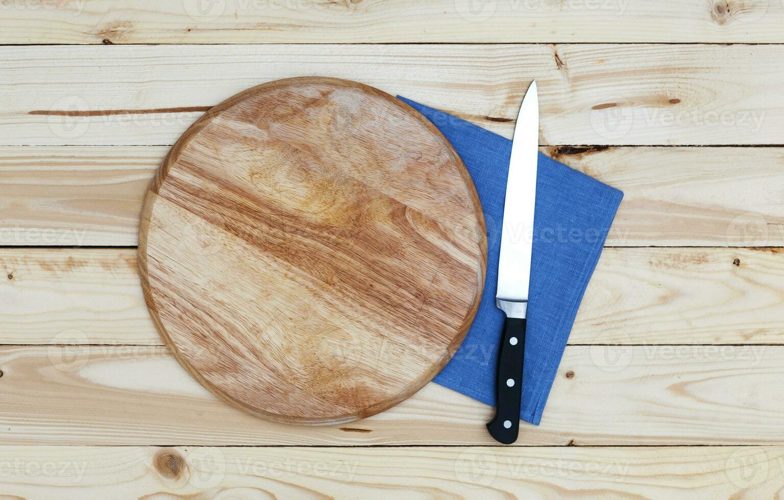 Round cutting board with a knife on a wooden table, top view photo