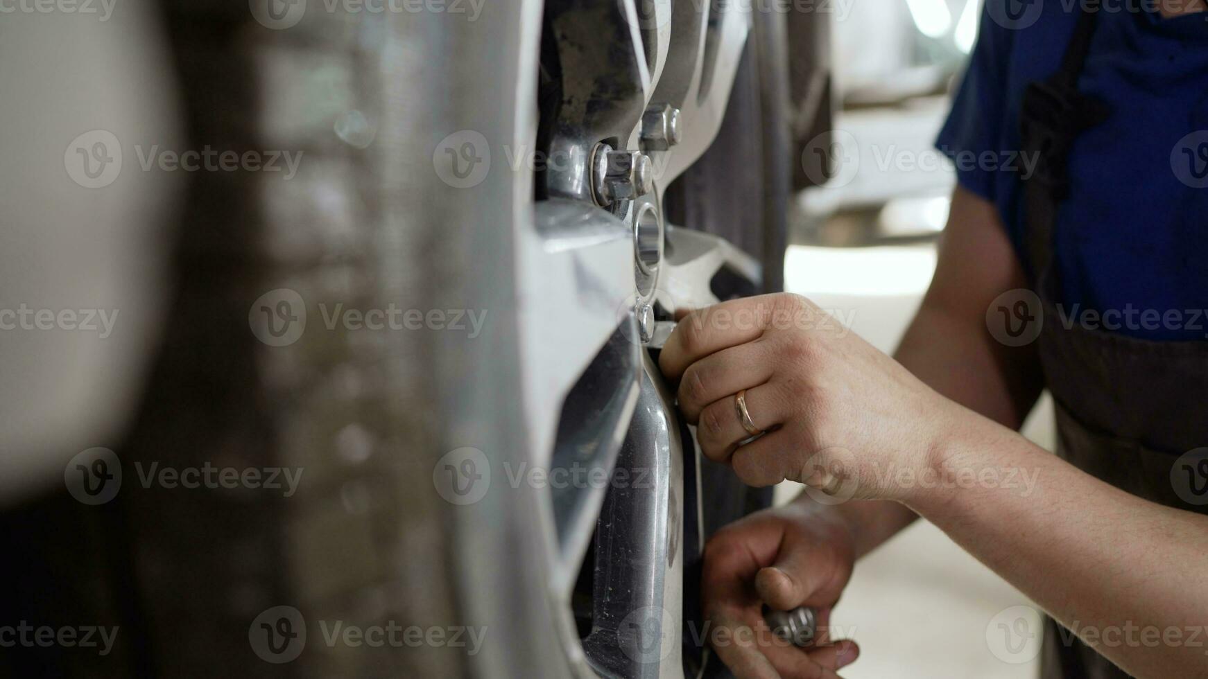 Car wheel replacement in workshop, self service tire fitting concept, handyman uses professional wrench to tighten wheel nuts. The master tightens the car wheel with a nut. photo