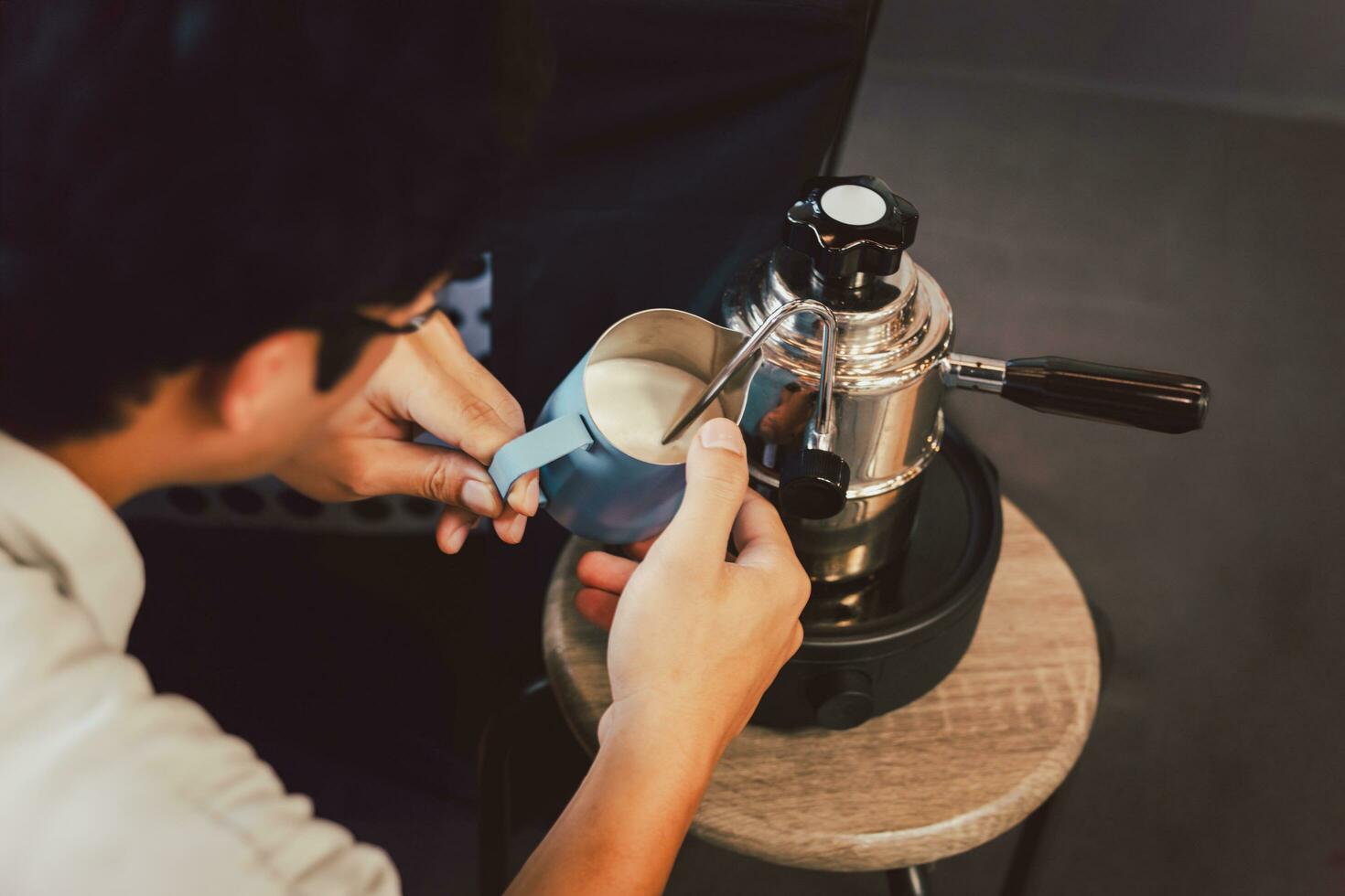 Man warming milk In metal jug with steam coffee machine at camping outdoor. photo