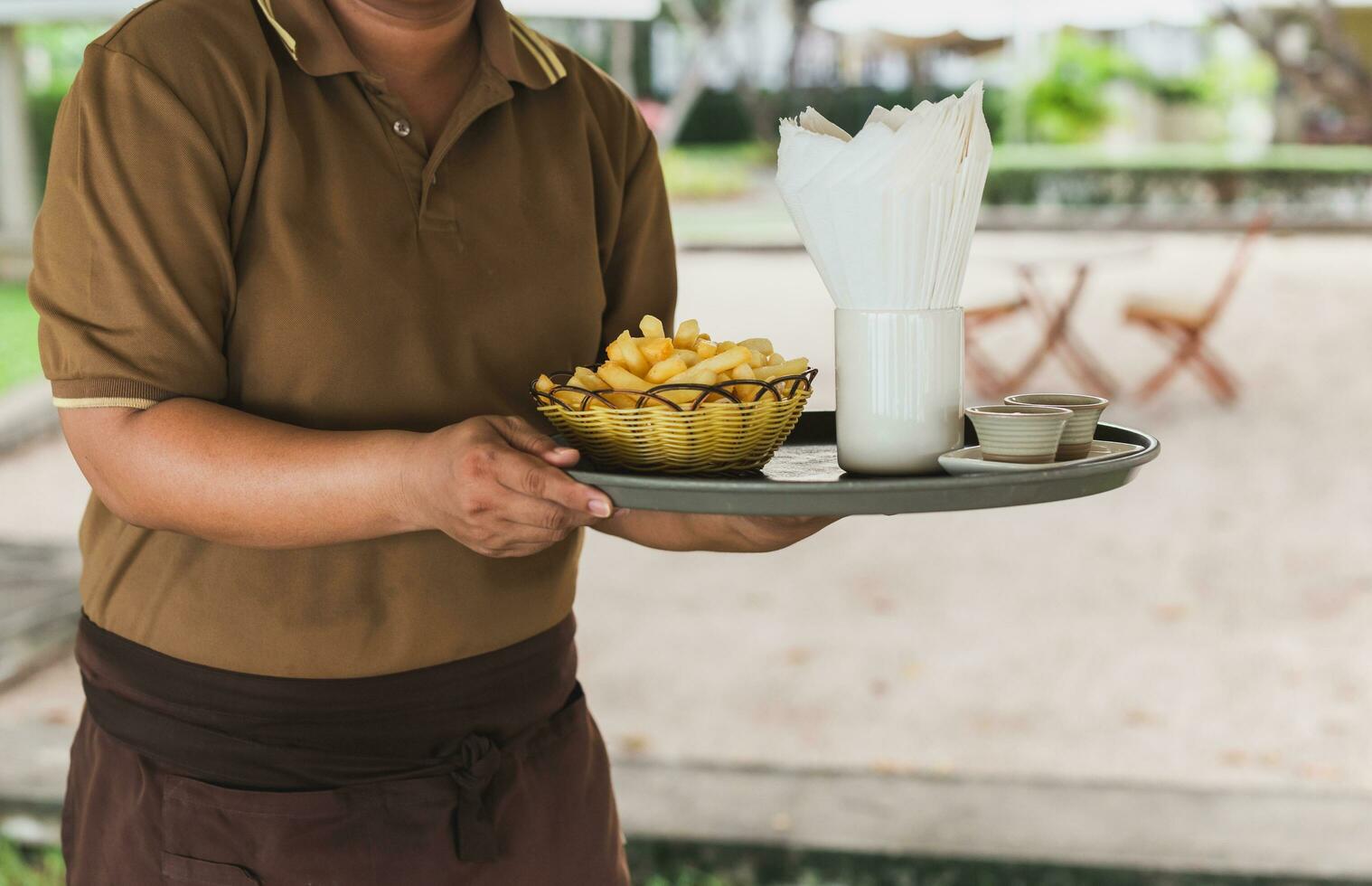 Waitress serving french fries in tray at restaurant outdoors. photo