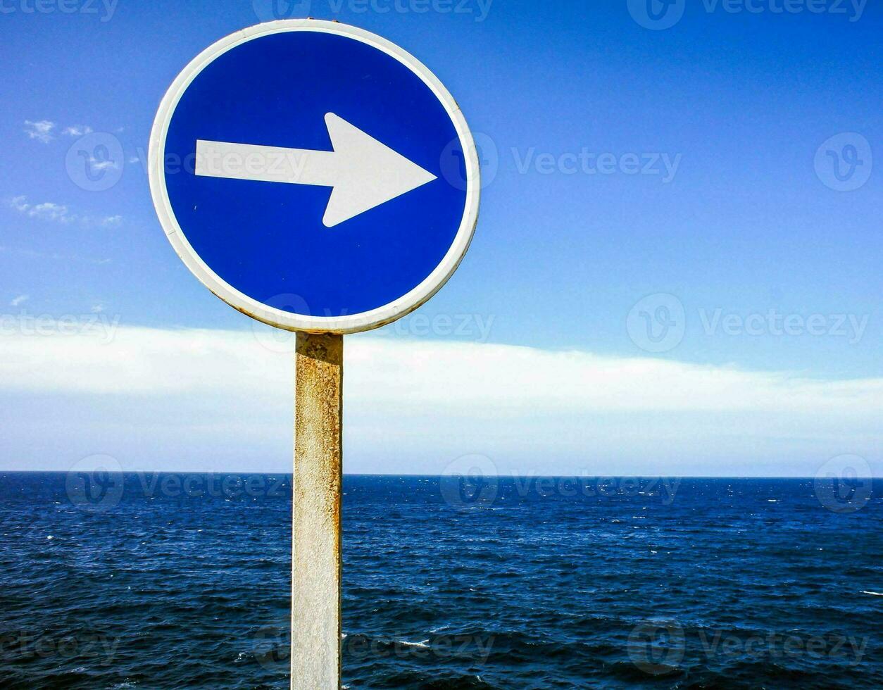 a blue and white sign pointing to the ocean photo