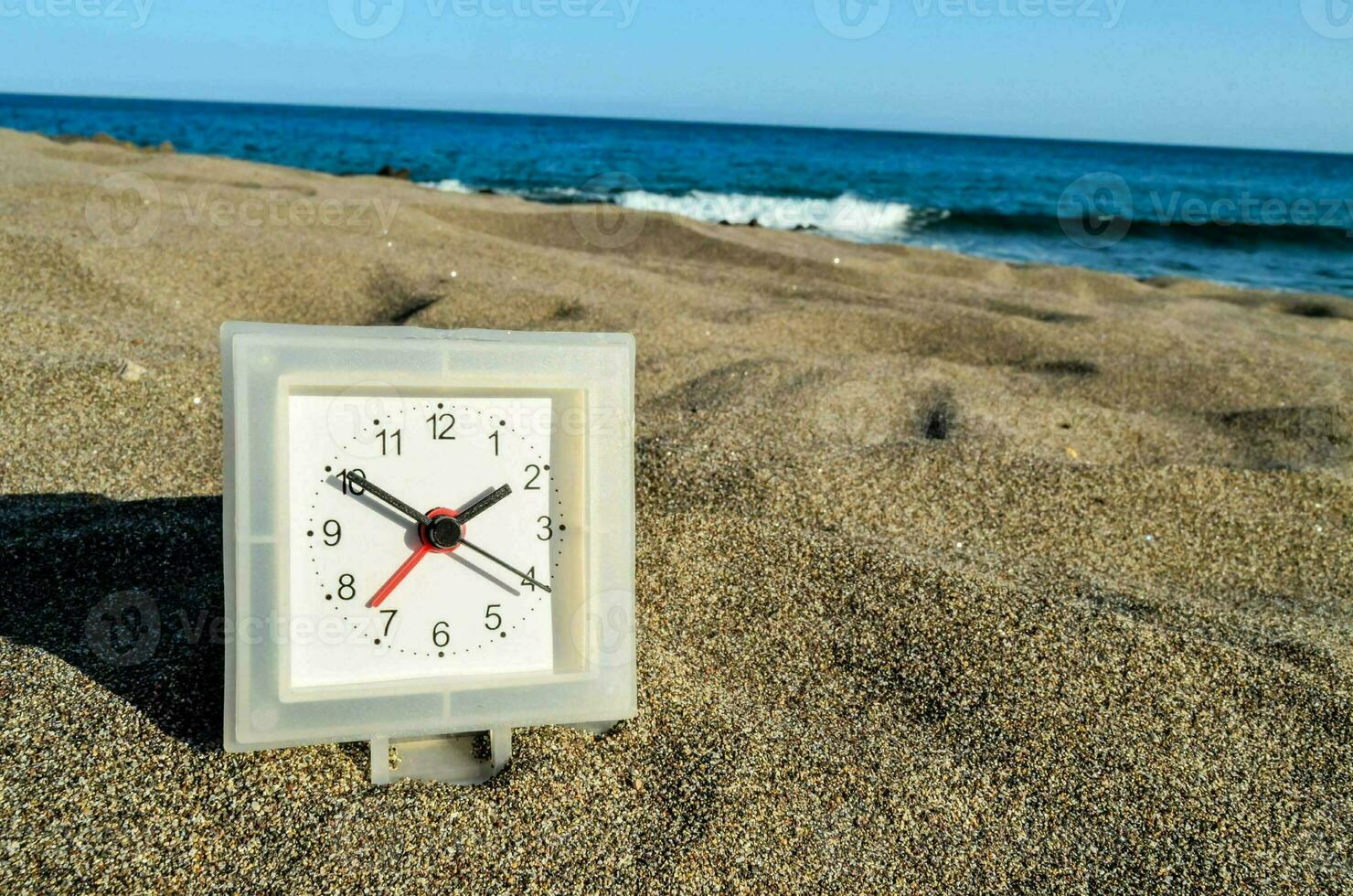 a clock on the beach with the ocean in the background photo