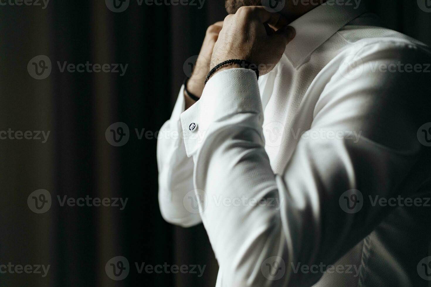 Close up cropped picture of caucasian male adjusting collar of a white shirt. Groom preparing for wedding. photo