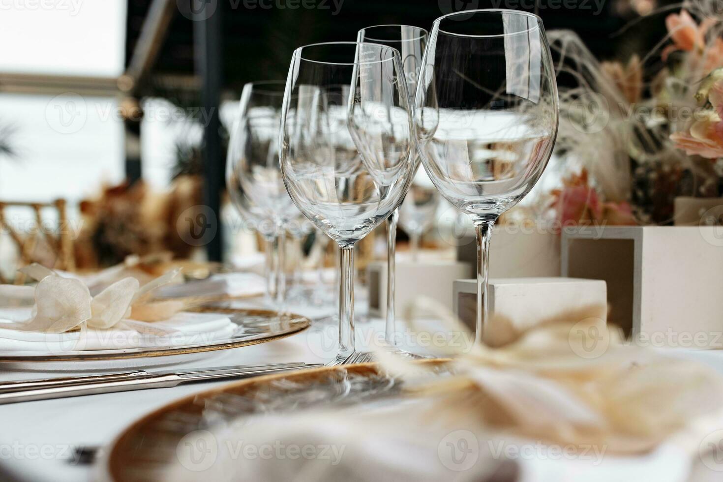 Transparent wine glasses on white tablecloth with plates and cutlery. Luxury restaurant close up view. photo