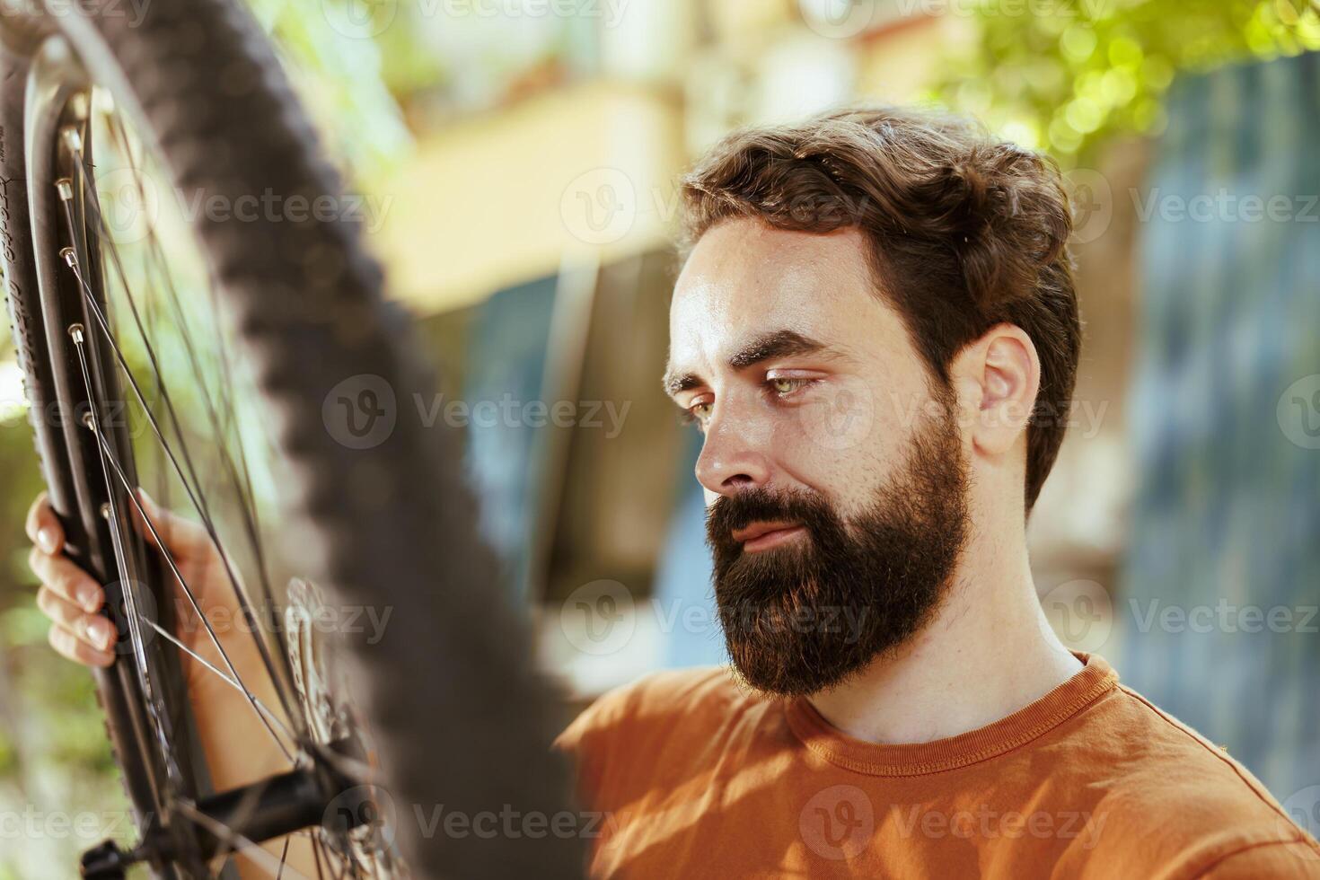 Active male cyclist checking tire as yearly bike rubber maintenance routine. Detailed image of enthusiastic sporty caucasian man gripping and examining damaged bicycle wheel for dismantle. photo
