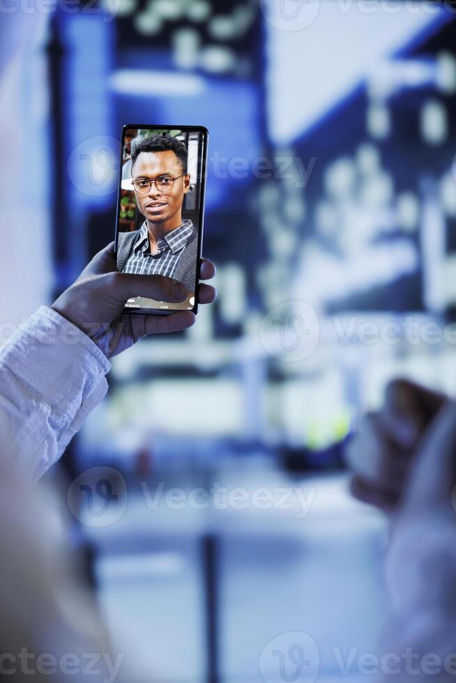 Woman in videocall with husband while walking around city streets at night, close up. Citizen using smartphone to show spouse surroundings in dimly illuminated urban center in blurry background photo