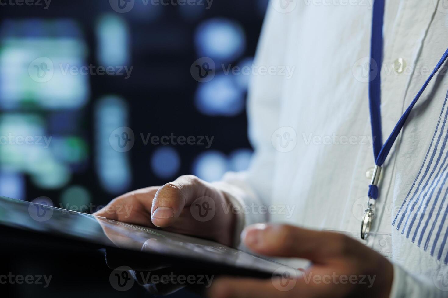 Engineer in data center using tablet to prevent system overload, close up. Employee in server room ensuring there is enough network connectivity for smooth operations, blurry background photo