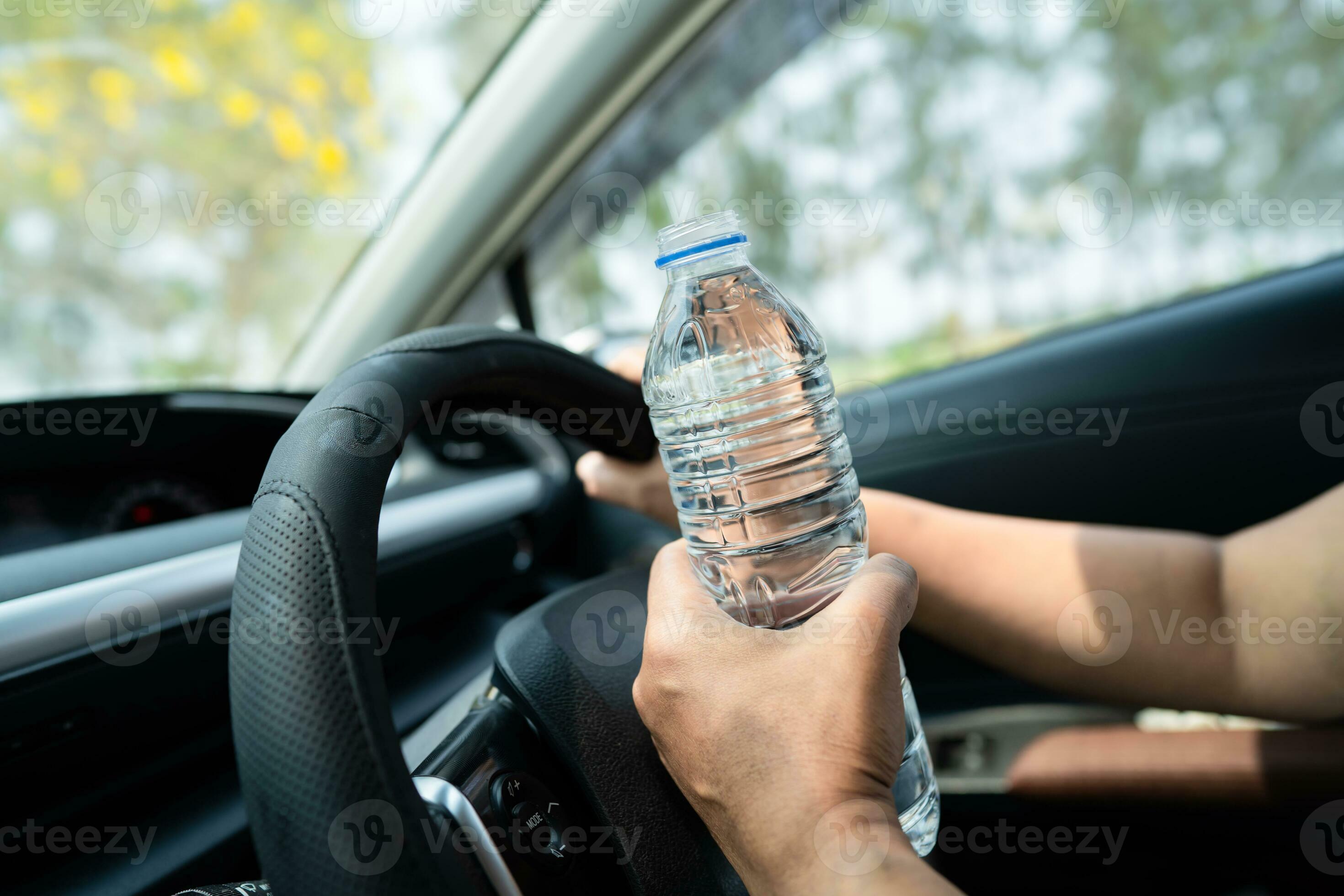 Asian woman driver holding bottle for drink water while driving a car. Plastic hot water bottle