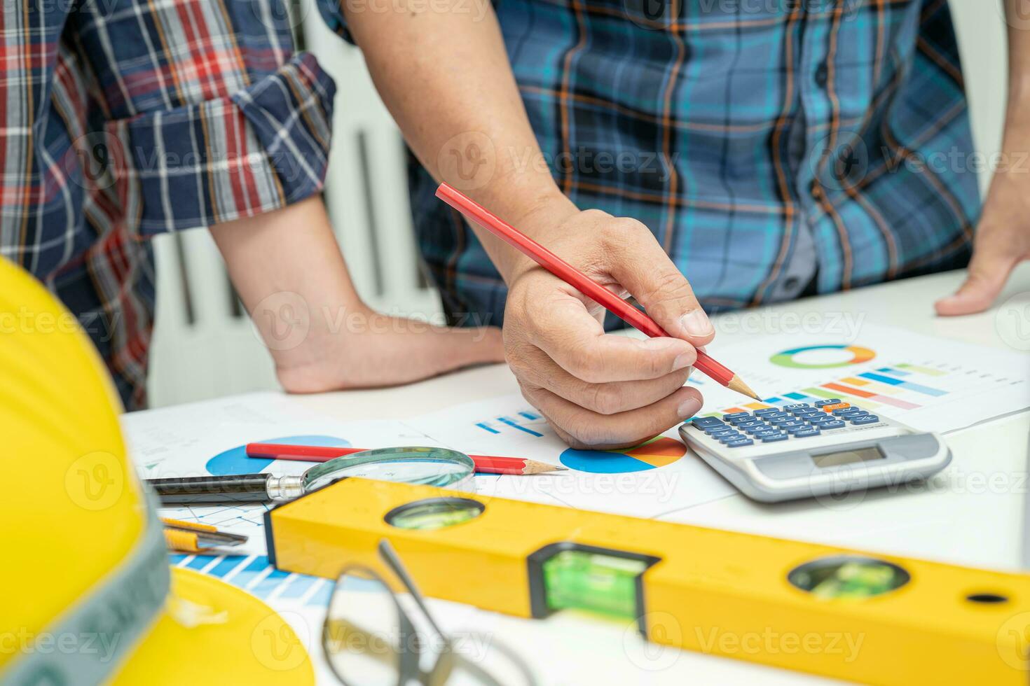 Asian engineer and partner team learn and talk with house plan project blueprint, graph and yellow helmet and engineering construction tools on table work. photo