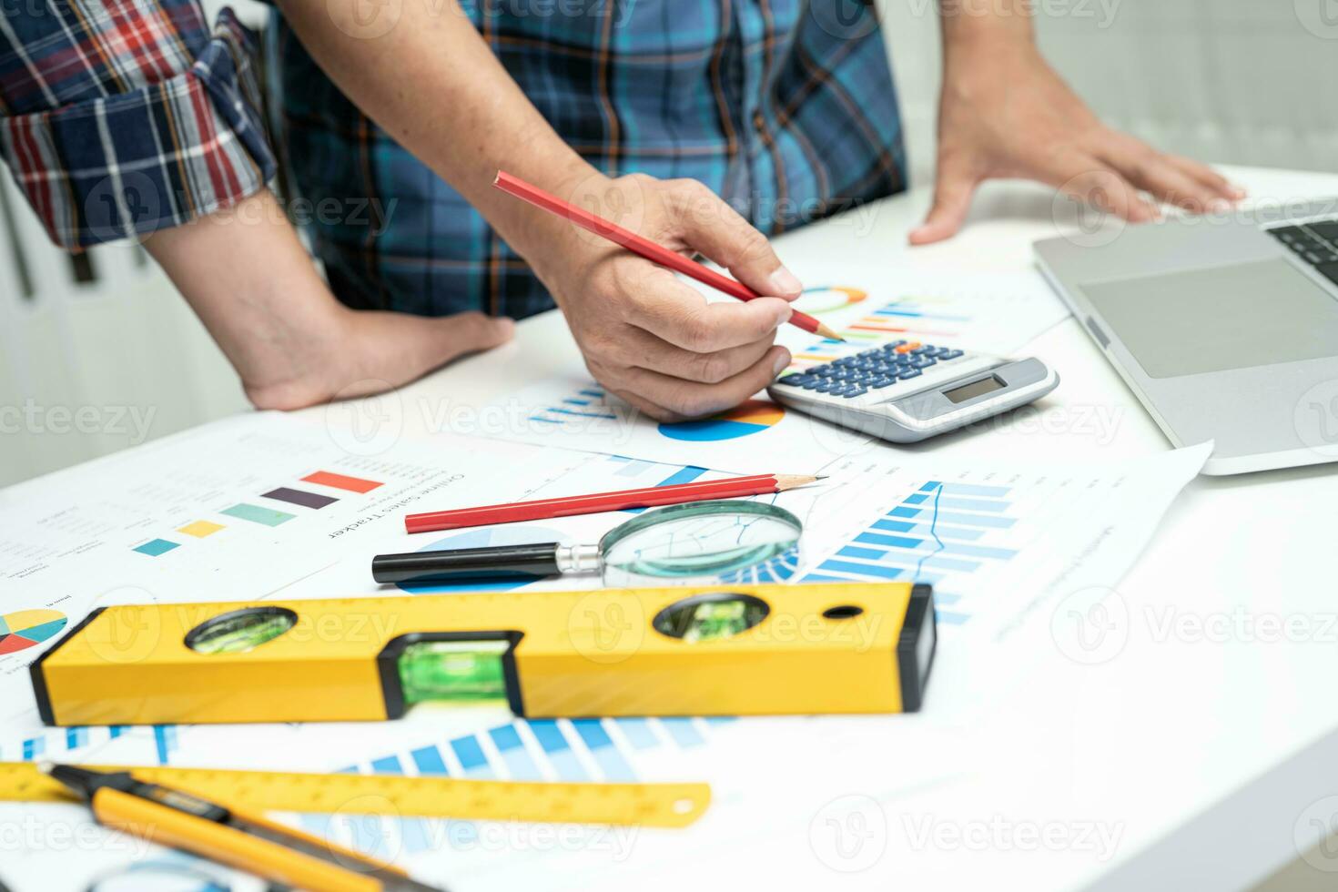Asian engineer and partner team learn and talk with house plan project blueprint, graph and yellow helmet and engineering construction tools on table work. photo