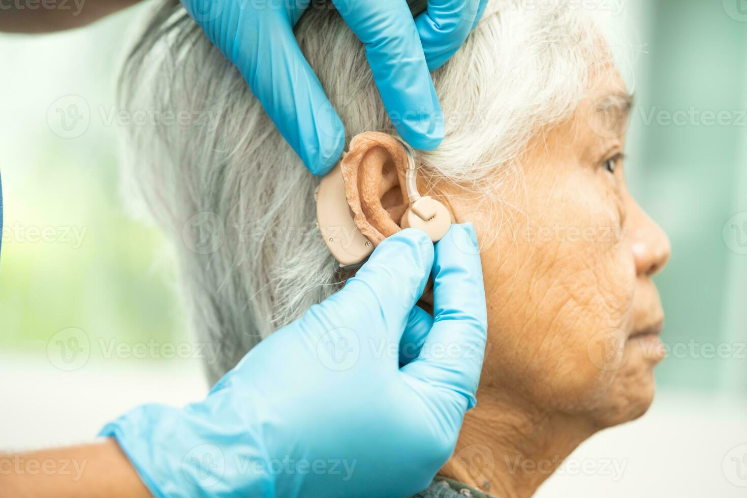 asiático mayor mujer paciente vistiendo un escuchando ayuda para tratando escuchando pérdida problema. foto