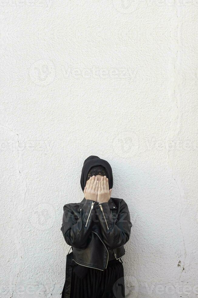 Young Muslim girl covering face with palms. Victim of domestic violence and abuse. Arabian woman hiding her face with hands and feeling ashamed photo