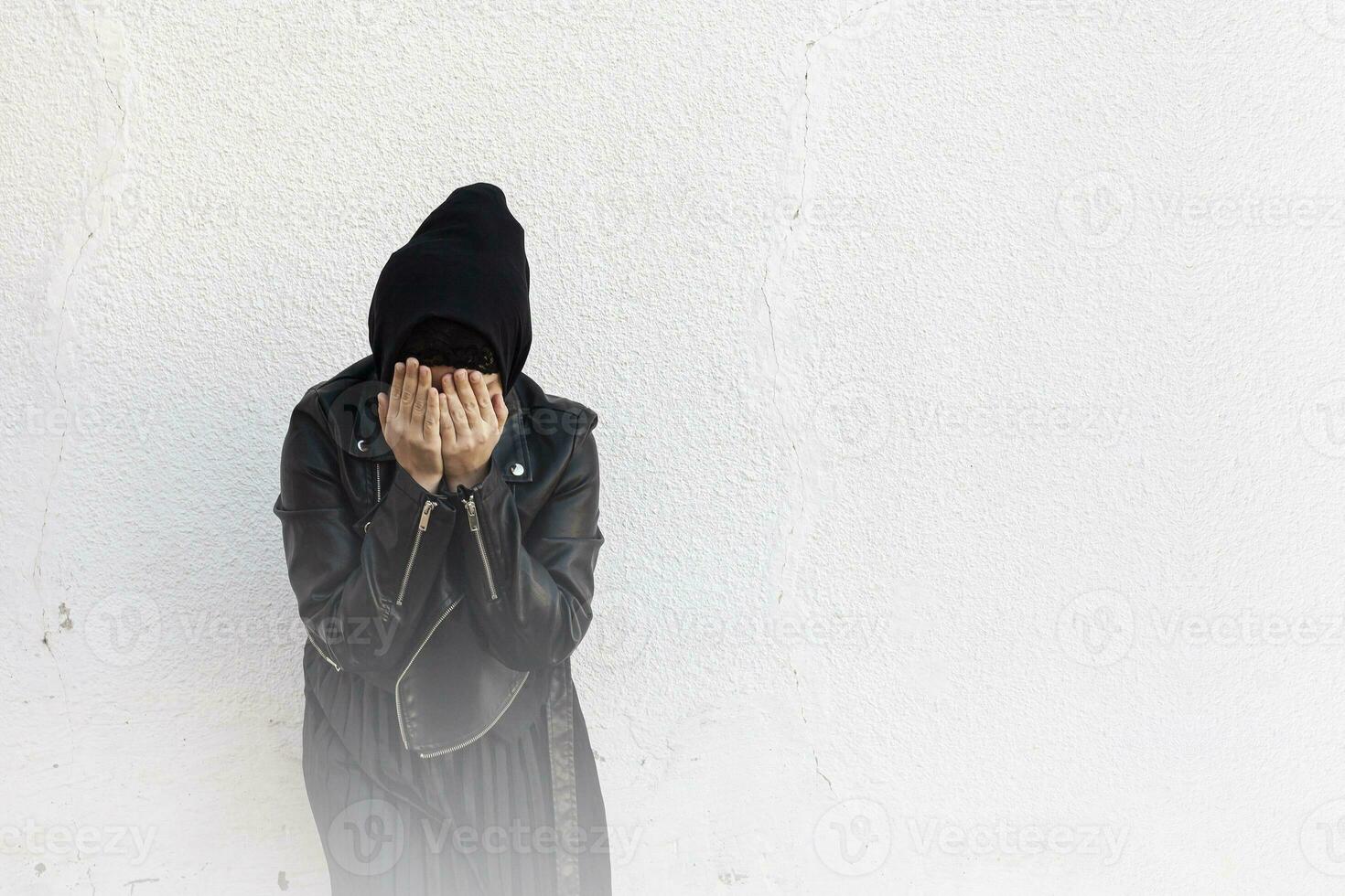Young Muslim girl covering face with palms. Victim of domestic violence and abuse. Arabian woman hiding her face with hands and feeling ashamed photo