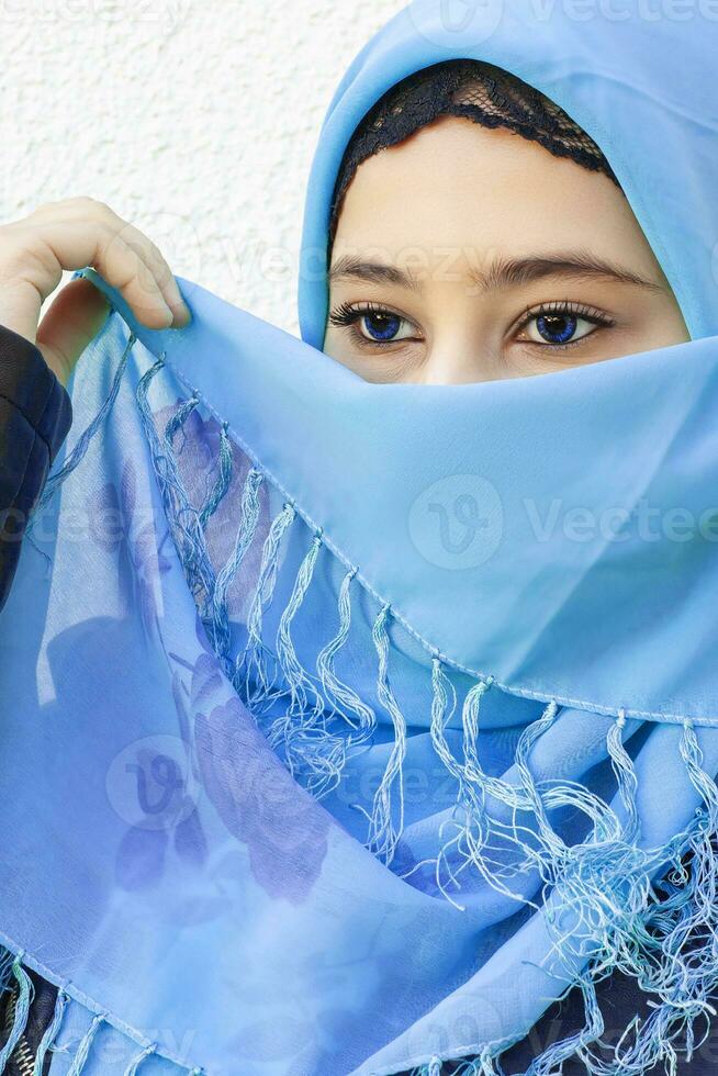 de cerca retrato de hermosa iraní niña con azul ojos. atractivo musulmán mujer en hijab cubierta su cara con bufanda foto