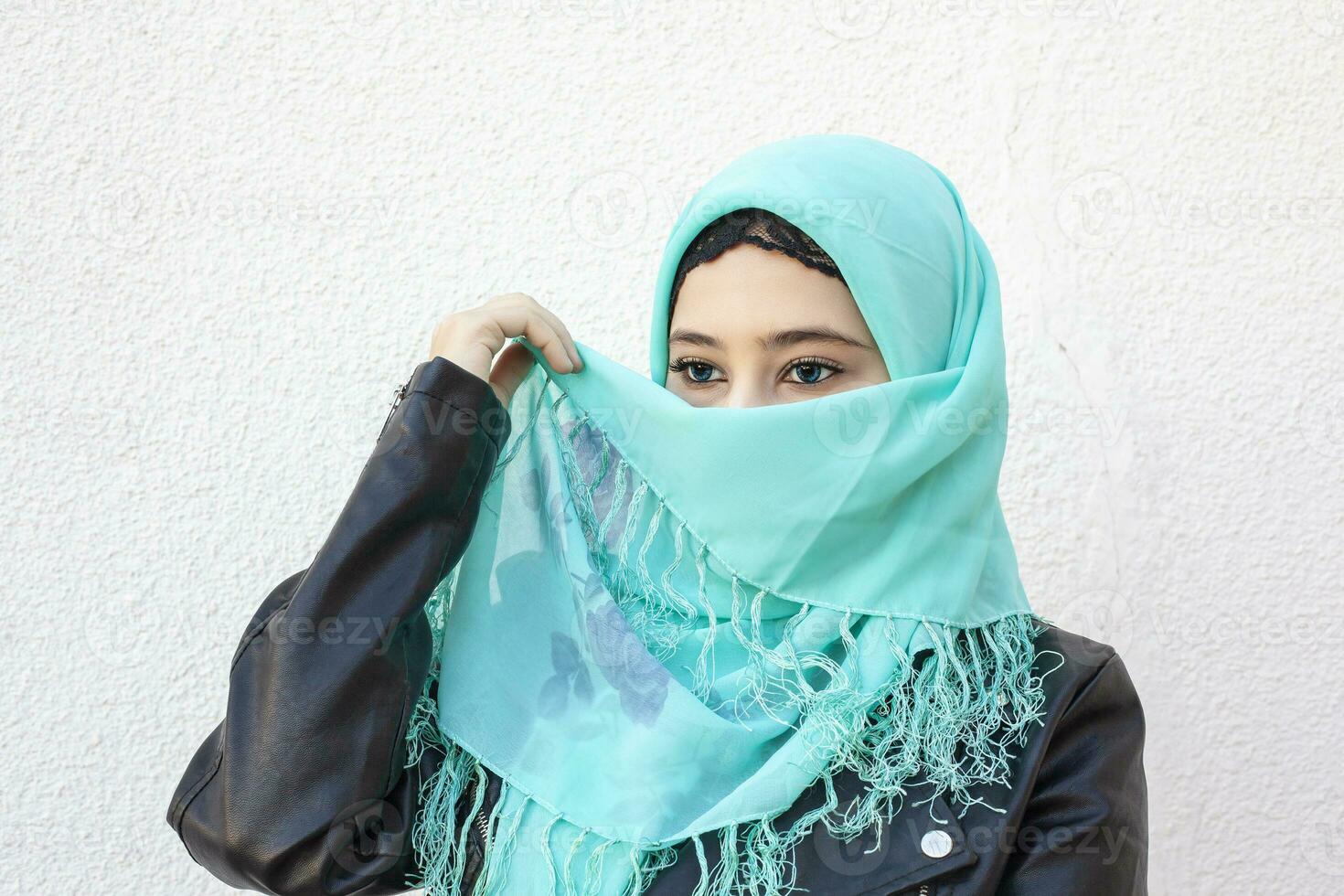 Close-up portrait of beautiful iranian girl with blue eyes. Attractive muslim woman in hijab covering her face with scarf photo