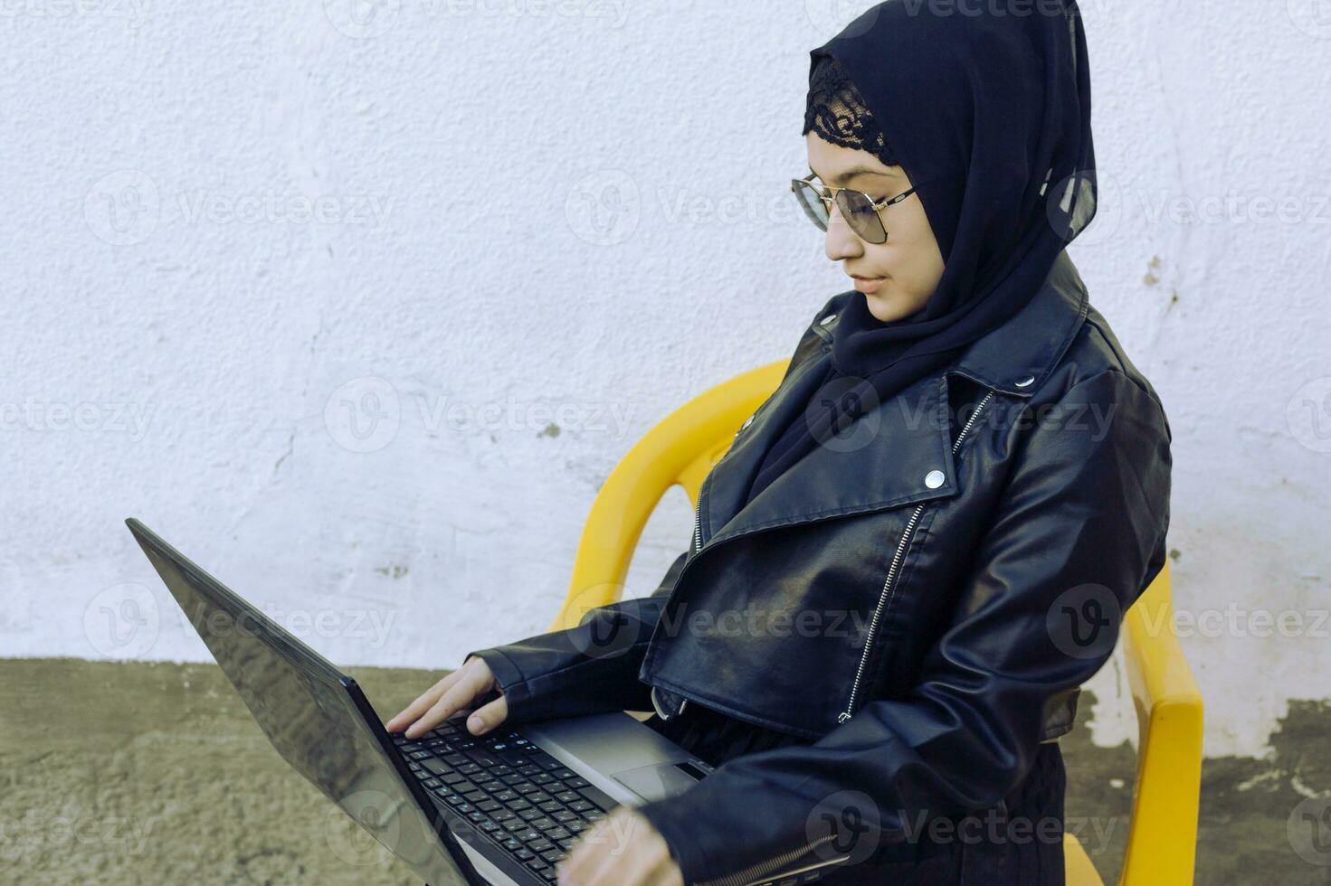 Beautiful middle-eastern working with the laptop. Cute Arabian Muslim woman in hijab posing with laptop outdoors. Blogger, vlogger, freelancer girl at the job process photo