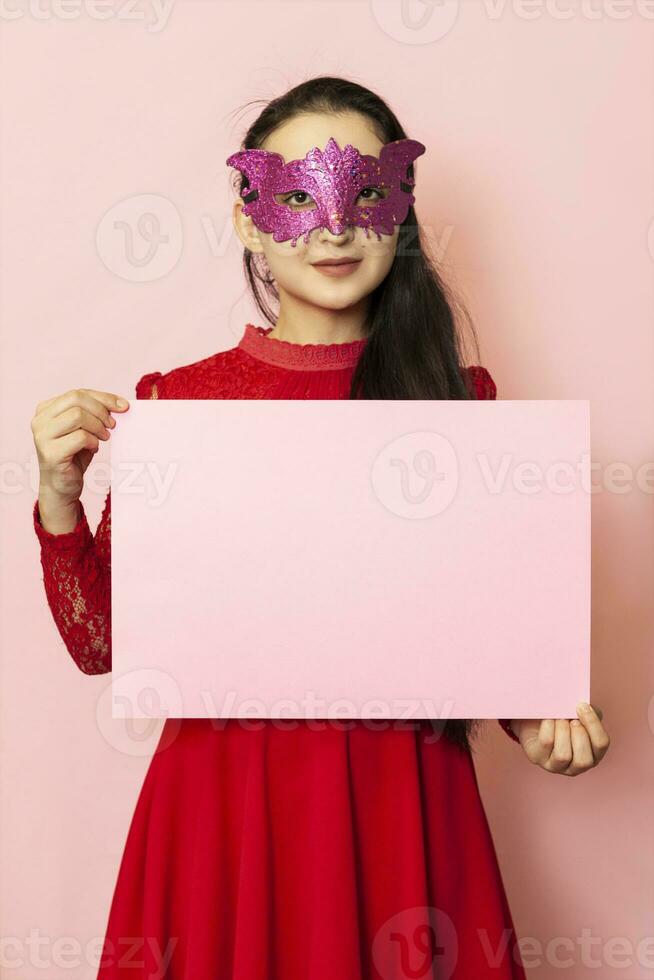 Young pretty woman in masquerade mask holding an empty card. 20s middle-eastern female holds blank paper. Advertisement, banner photo