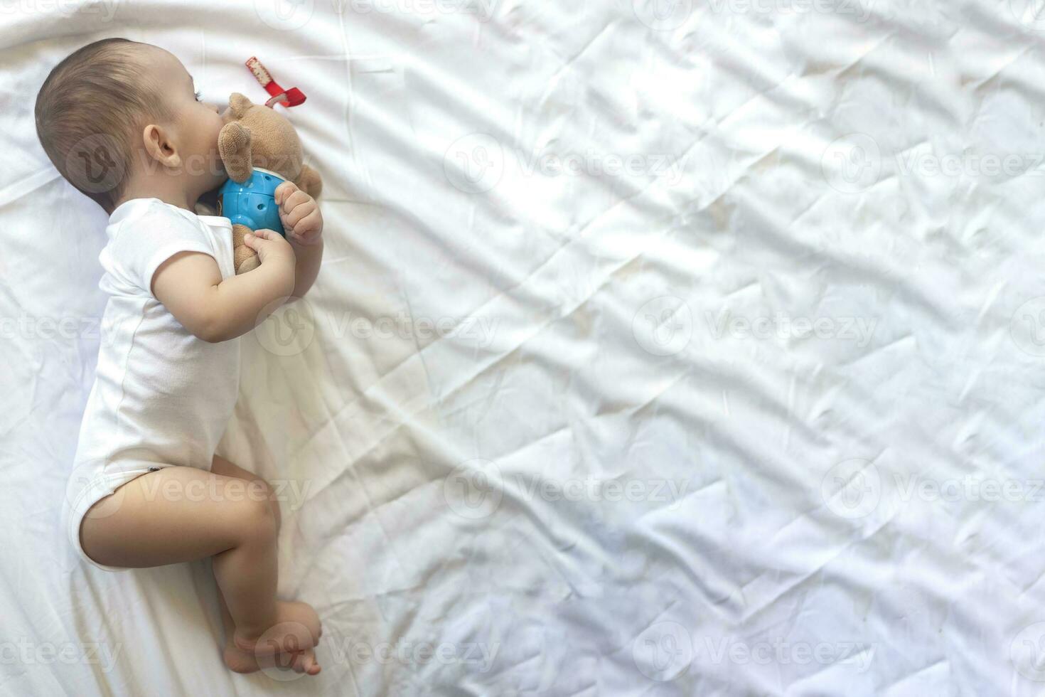 6-8-month-old baby boy lying playfully in bed. Charming 6-7 month little baby in white bodysuit. Baby boy in white bedding. Copy space photo