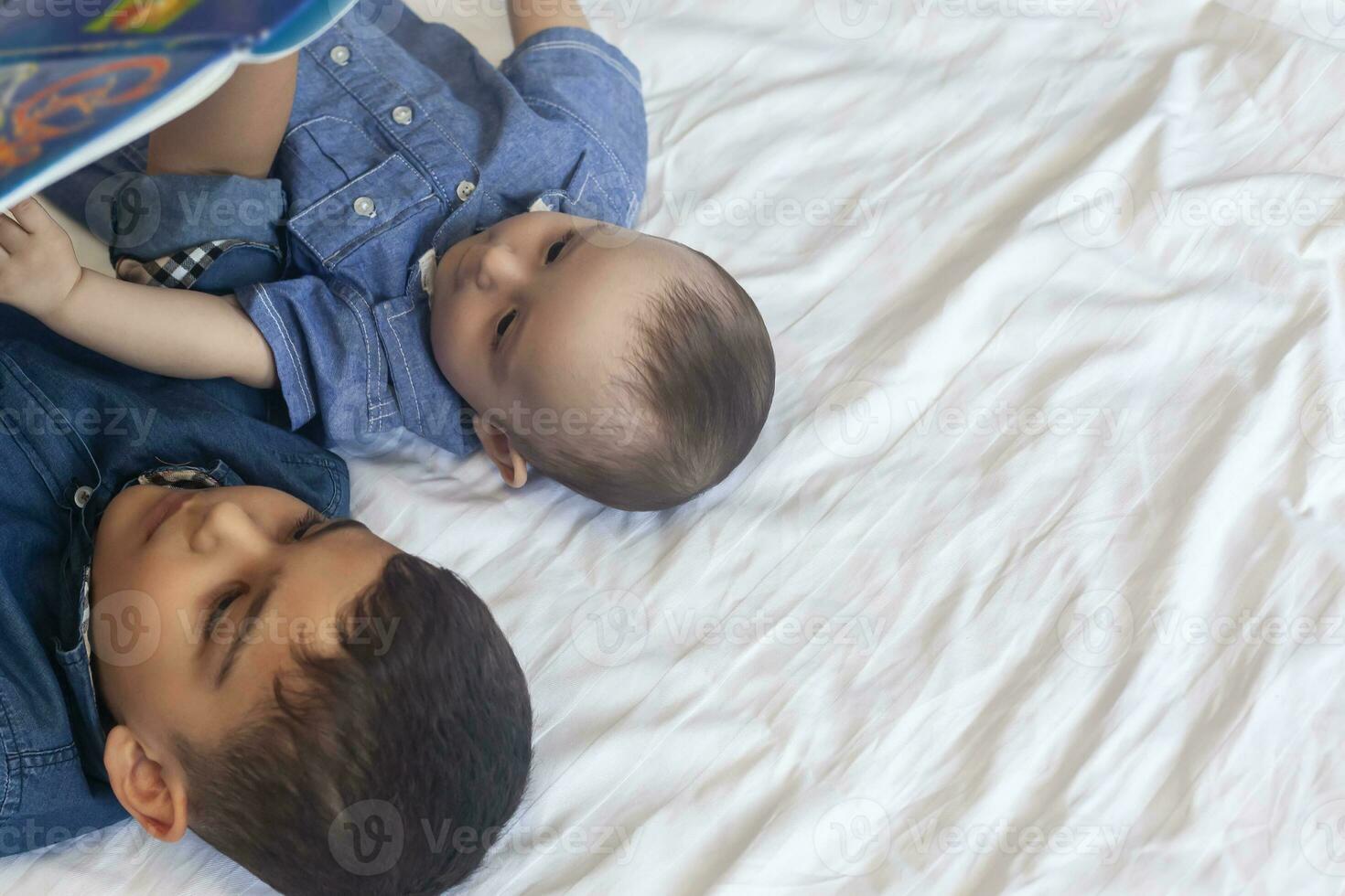 dos pequeño hermanos leyendo un libro. infantil niños acostado en el cama y leer el cuento antes de durmiendo. leyendo un corto historia para niños. medio oriental niños en su cama. foto