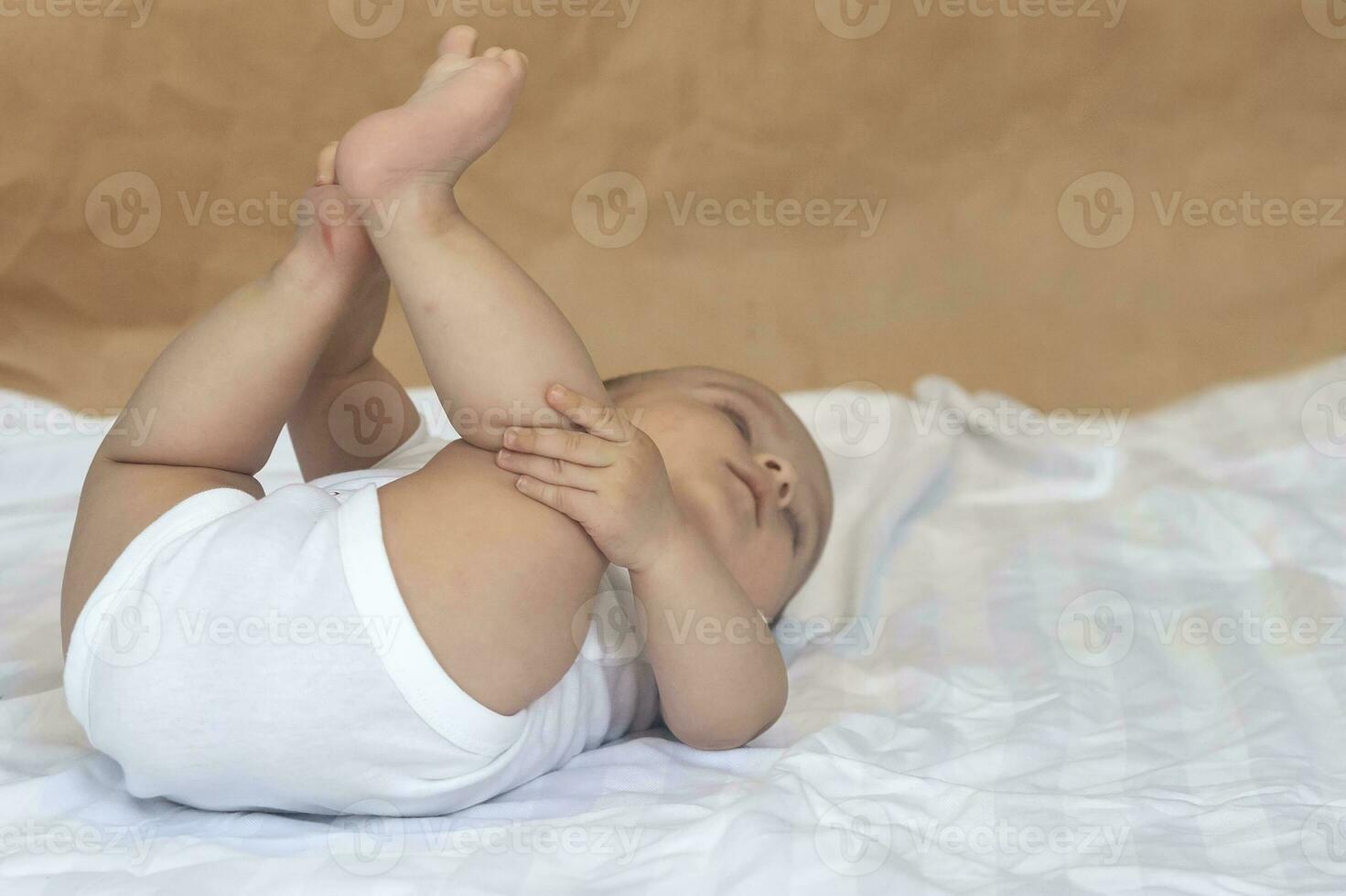 6-8-month-old baby boy lying playfully in bed. Charming 6-7 month little baby in white bodysuit. Baby boy in white bedding. Copy space photo