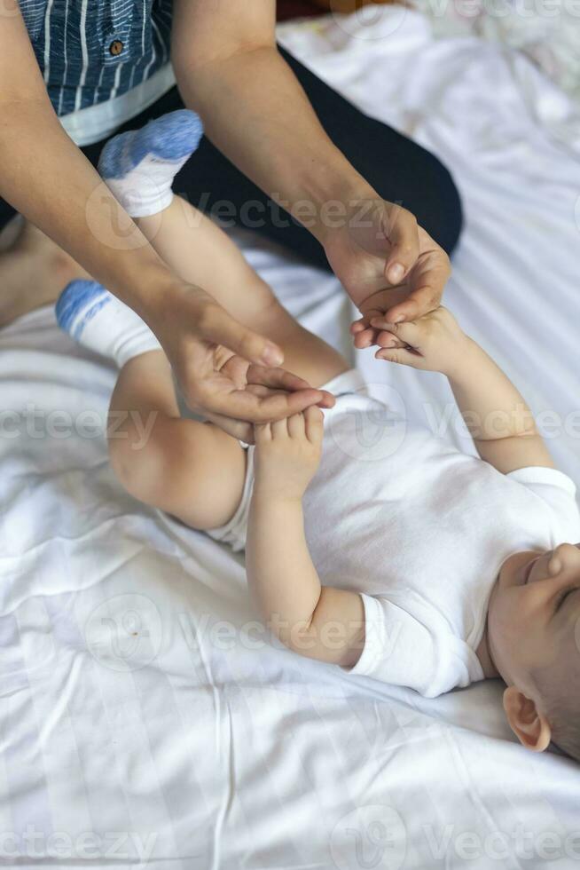 Baby massage. Mom doing gymnastics with kid. Mommy massaging cute baby boy. Moving baby's legs to help relieve constipation. Young mother doing exercises and movements to stimulate baby's bowels. photo