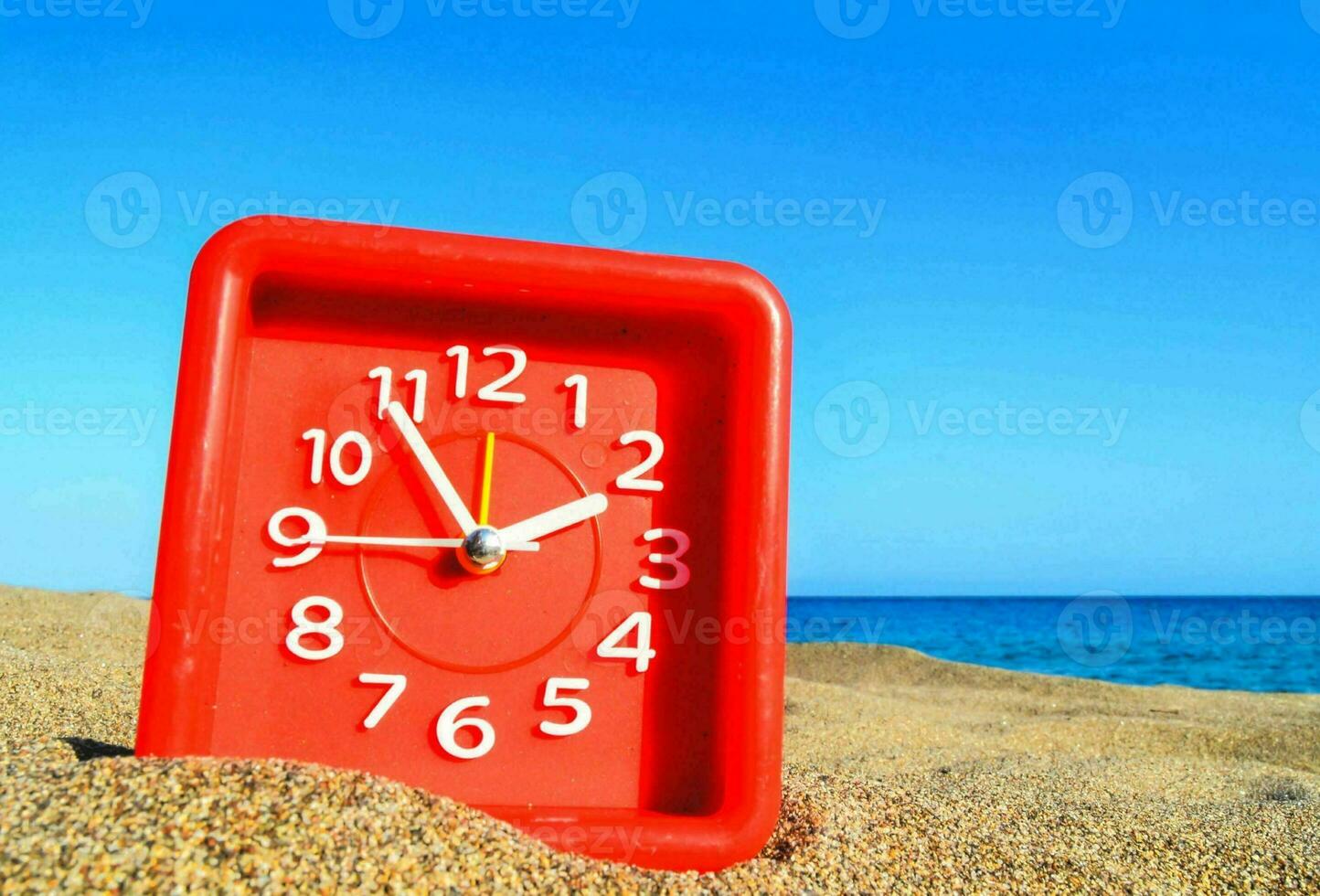 a red clock on the beach with the ocean in the background photo
