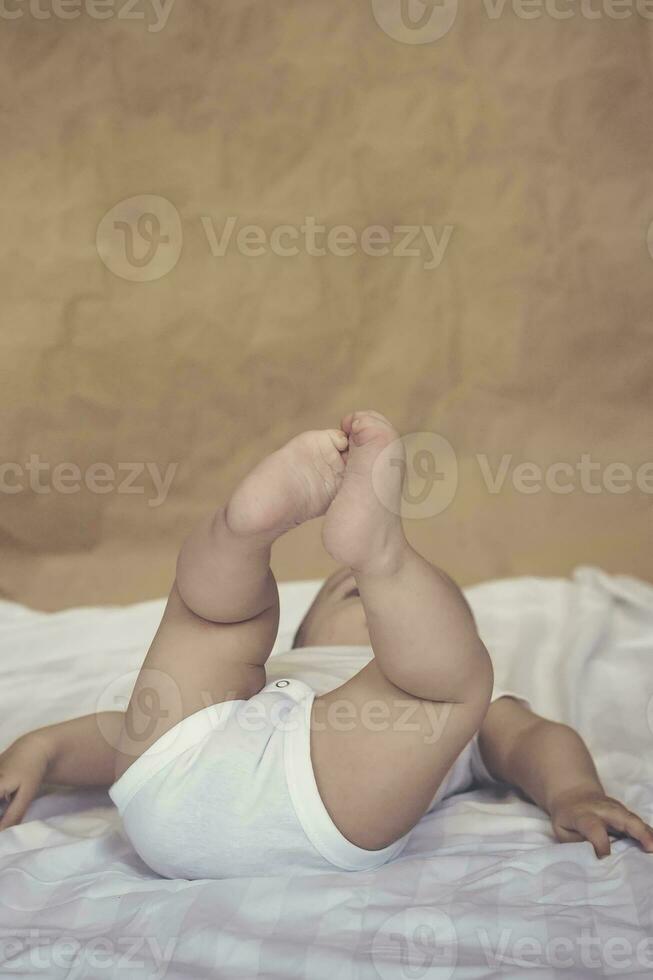 6-8 meses bebé chico acostado en broma en cama. encantador 6-7 mes pequeño bebé en blanco mono bebé chico en blanco lecho. Copiar espacio foto