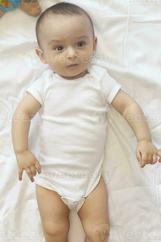 6-8-month-old baby boy lying playfully in bed. Charming 6-7 month little baby in white bodysuit. Baby boy in white bedding. Copy space photo