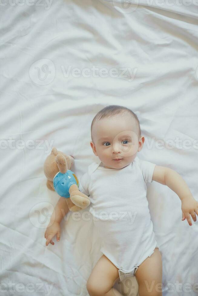 6-8-month-old baby boy lying playfully in bed. Charming 6-7 month little baby in white bodysuit. Baby boy in white bedding. Copy space photo