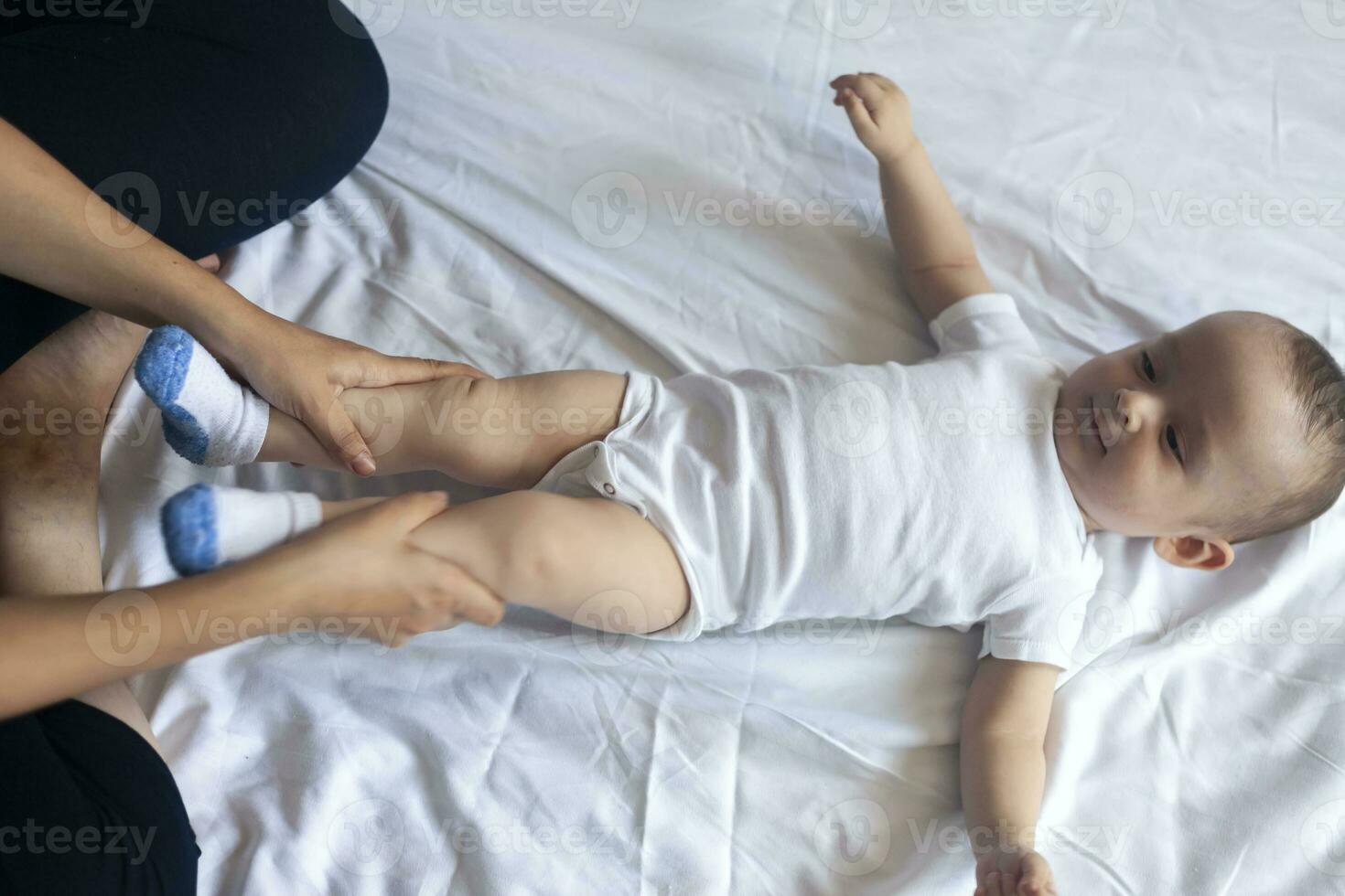 Baby massage. Mom doing gymnastics with kid. Mommy massaging cute baby boy. Moving baby's legs to help relieve constipation. Young mother doing exercises and movements to stimulate baby's bowels. photo