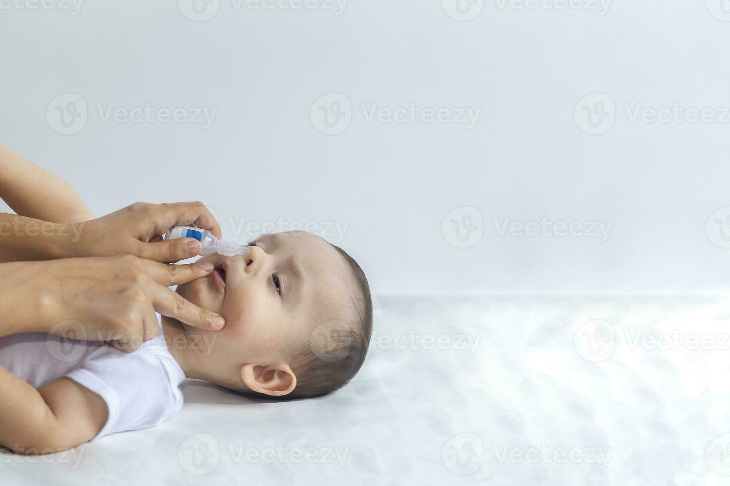 Little boy getting nasal drops. Pediatrician putting saline drops in infant's nose. Mother hands clearing the nose of baby. 6-month baby boy gets nose drops. photo