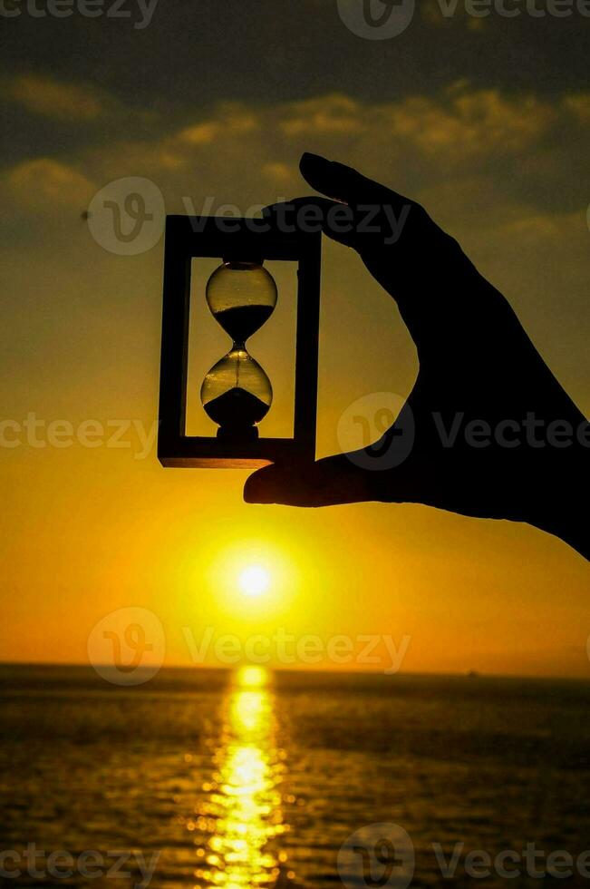 a person holding up a hourglass in front of the sunset photo