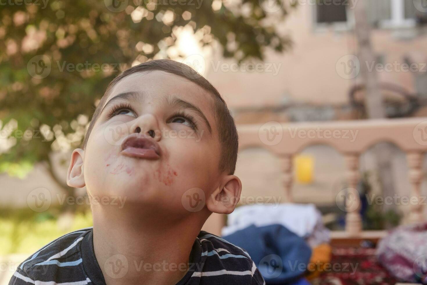 Little boy contorts his face at outdoors. 6 years old kid in summer holidays. Cute little boy fooling around. People, childhood lifestyle concept. Portrait of young child making funny faces photo