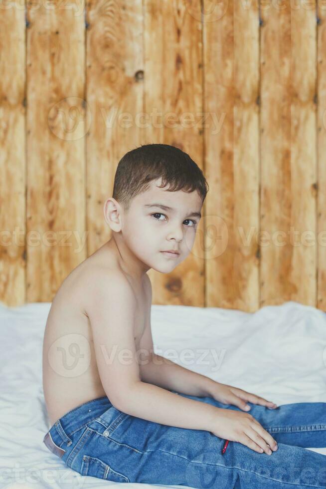 Happy childhood concept. 6 years old boyhaving good time. Cute little kid sitting on comforter photo