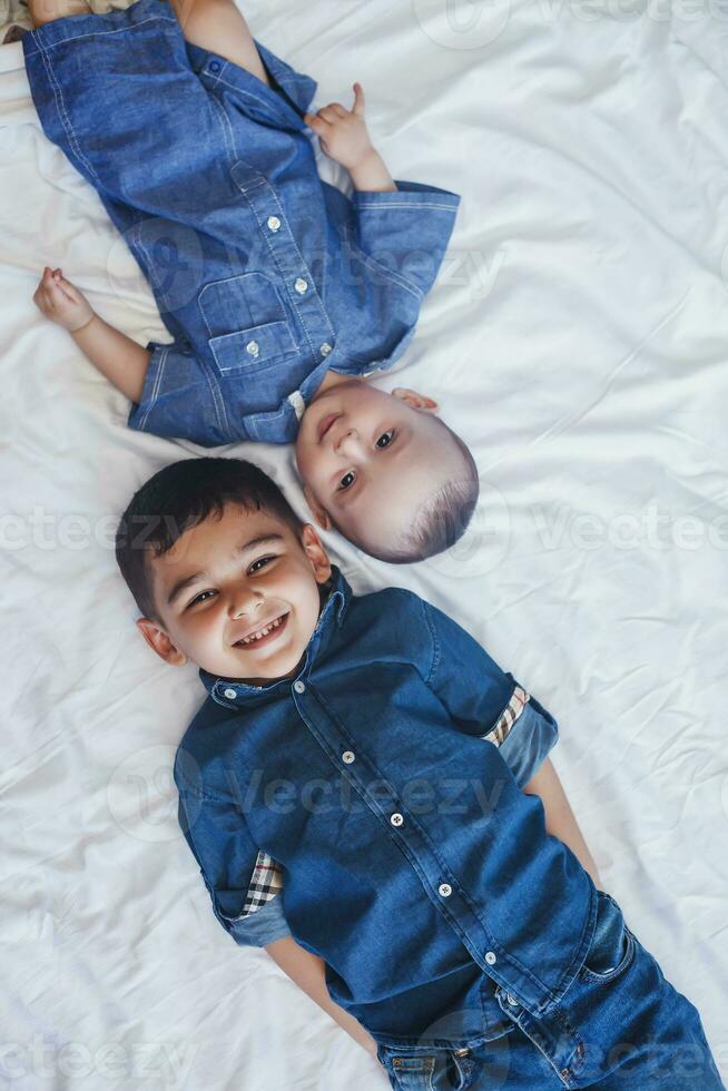 Happy childhood concept. Happy brothers portrait. 6 years boy and 6 months old baby boy having fun. Two little kids smiling to the camera. Cute little brothers lying on bed together photo