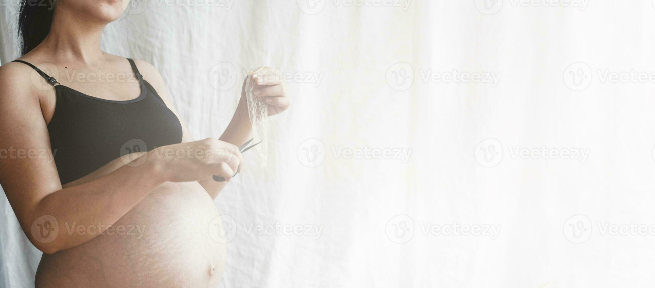 Pregnant woman cutting a condom photo