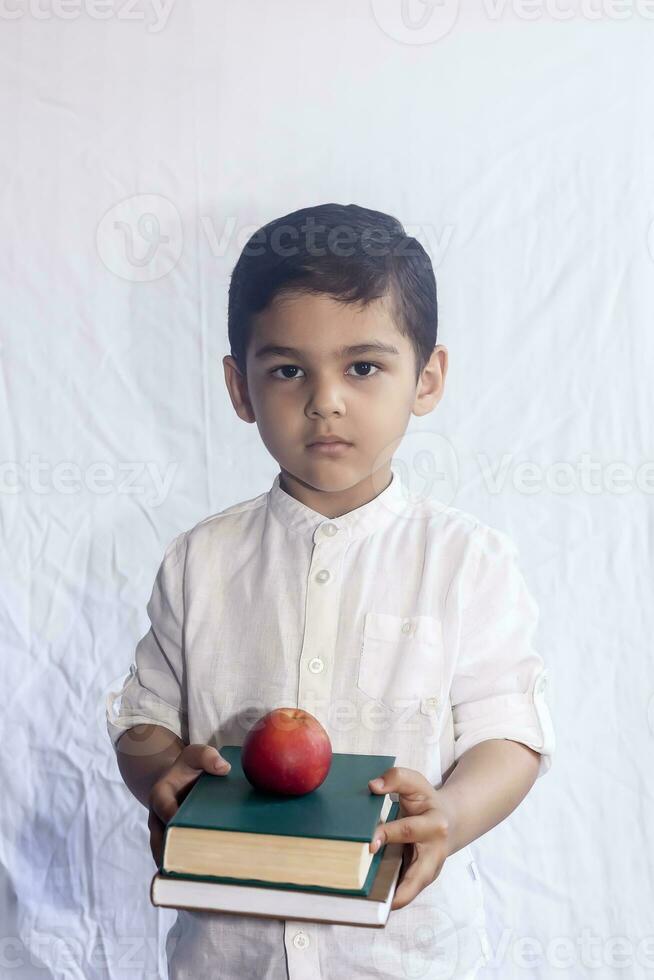 Back to school concept. Cute middle eastern boy holding a stack of books against the white background. Portrait of Central Asian kid preparing to go to school photo