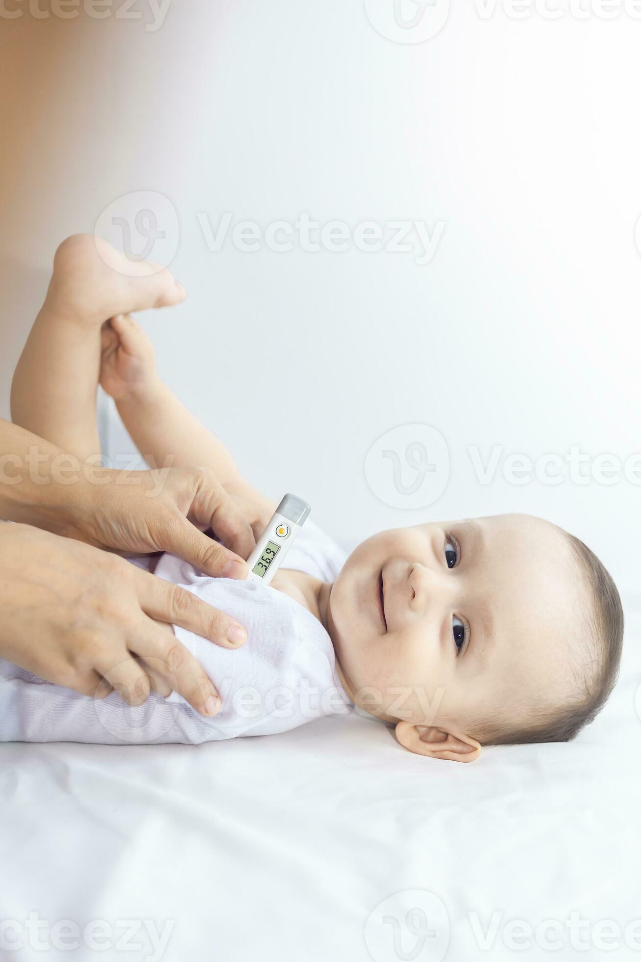Happy baby boy feeling well after the illness. Young mother using thermometer to take baby's