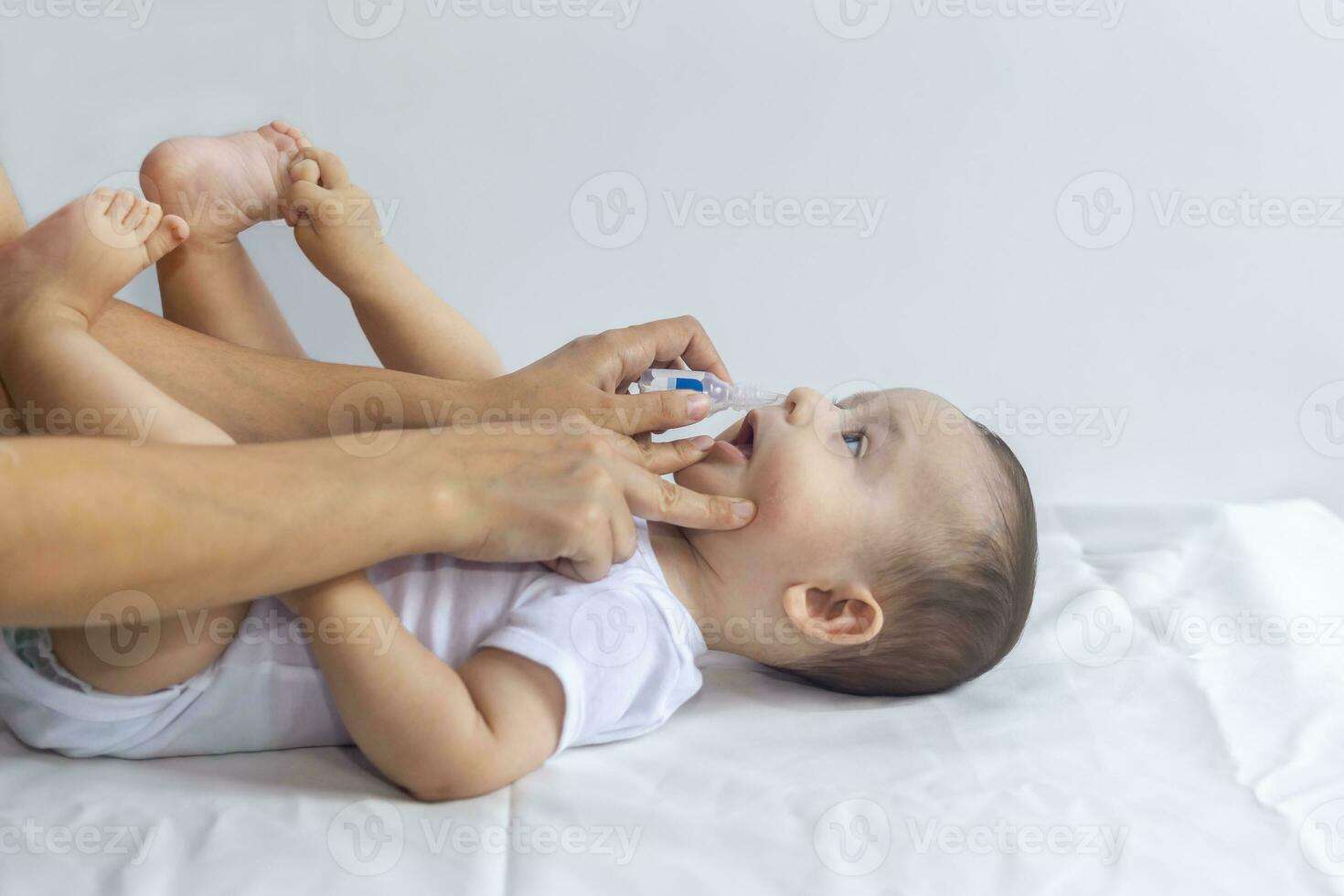 Little boy getting nasal drops. Pediatrician putting saline drops in infant's nose. Mother hands clearing the nose of baby. 6-month baby boy gets nose drops. photo