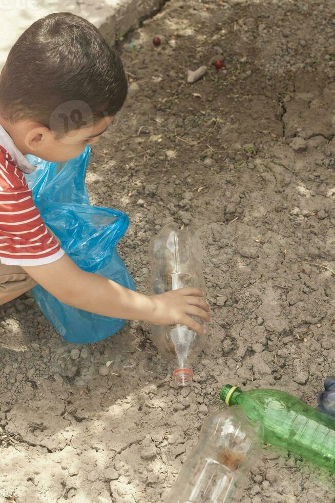 Plastic pollution on land. Little boy collecting plastic bottles. Kid carry garbage bag. Free space photo